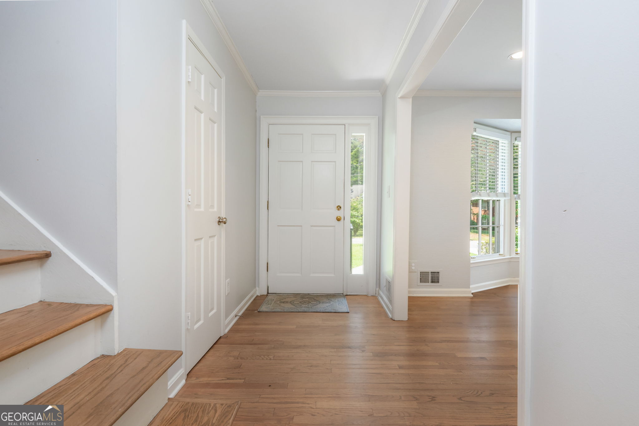 Entry foyer with hardwood floors, a white front door, and a wood-tread staircase.
