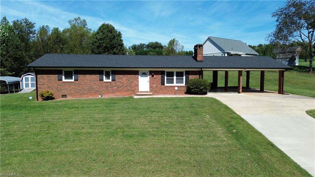 Red brick ranch house with a long carport and broad lawn.