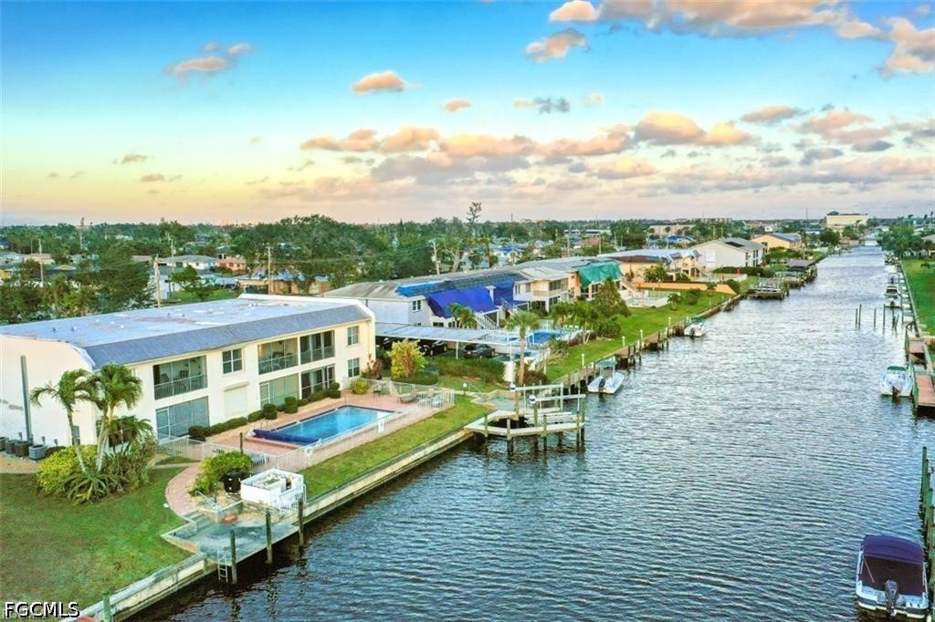 Waterfront condominiums line a canal, with docks, boats, and a pool under a colorful evening sky.