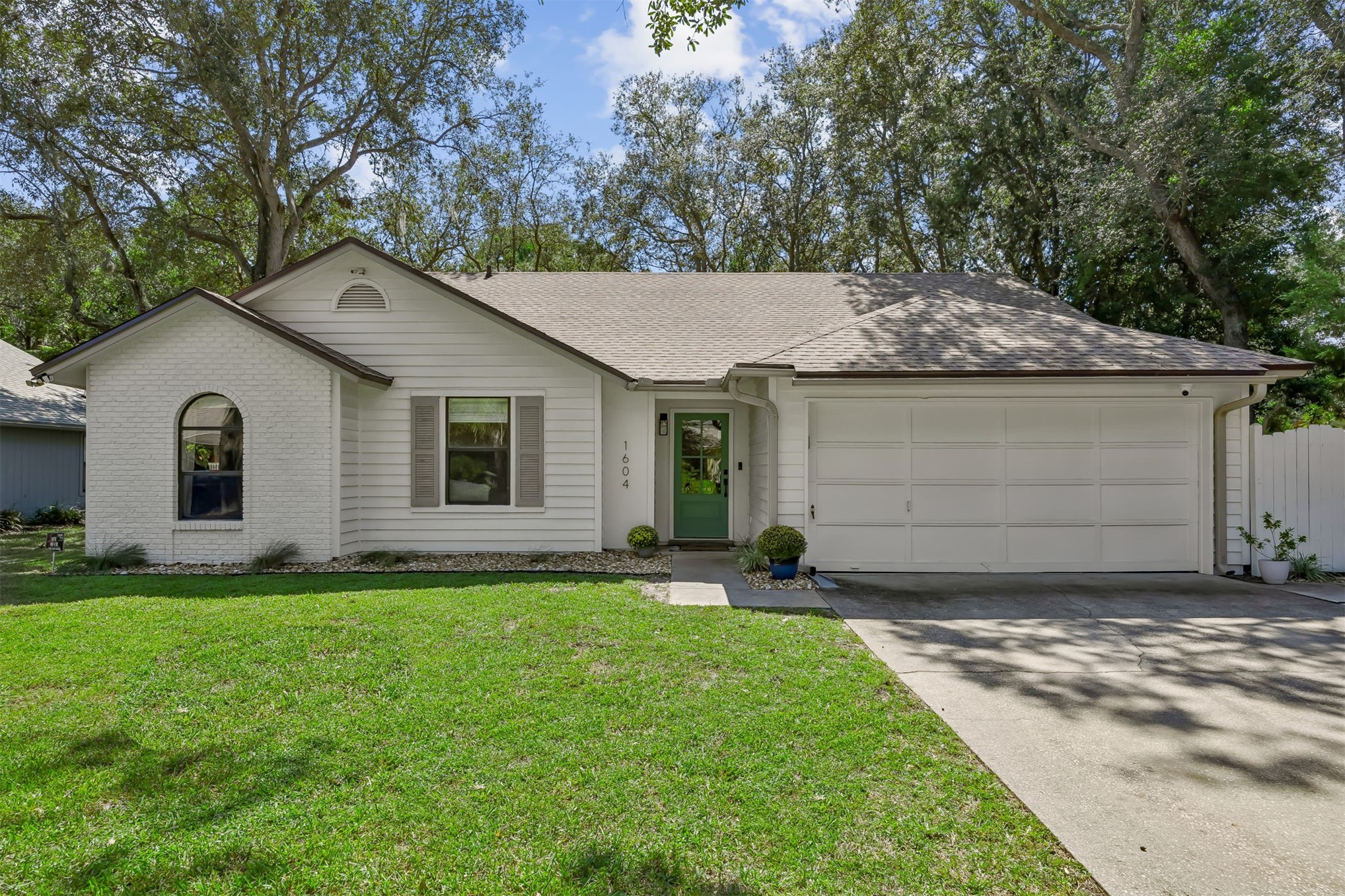 White single-story house with a green front door, attached garage, and mature trees.