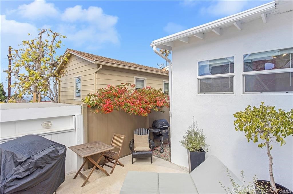 Backyard patio with a small dining set, covered barbecue, and flowering vines along the fence.