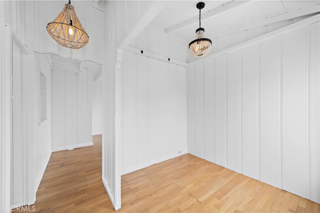 Empty white-paneled room with hardwood floors and two decorative pendant lights.
