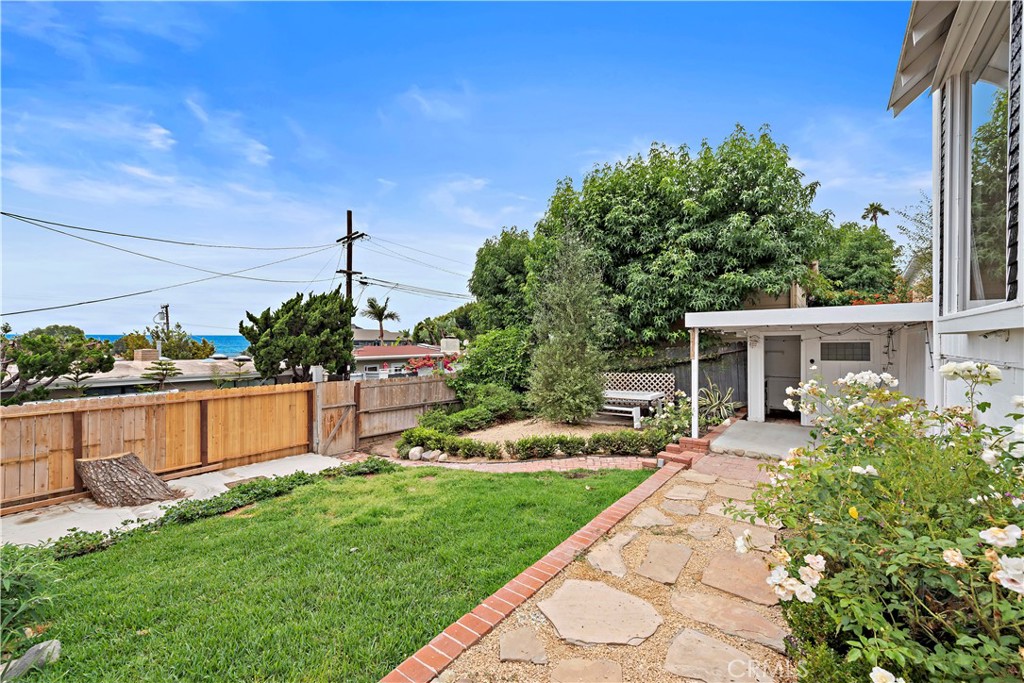 Backyard with a flagstone path, covered patio, lawn, and a glimpse of the ocean.