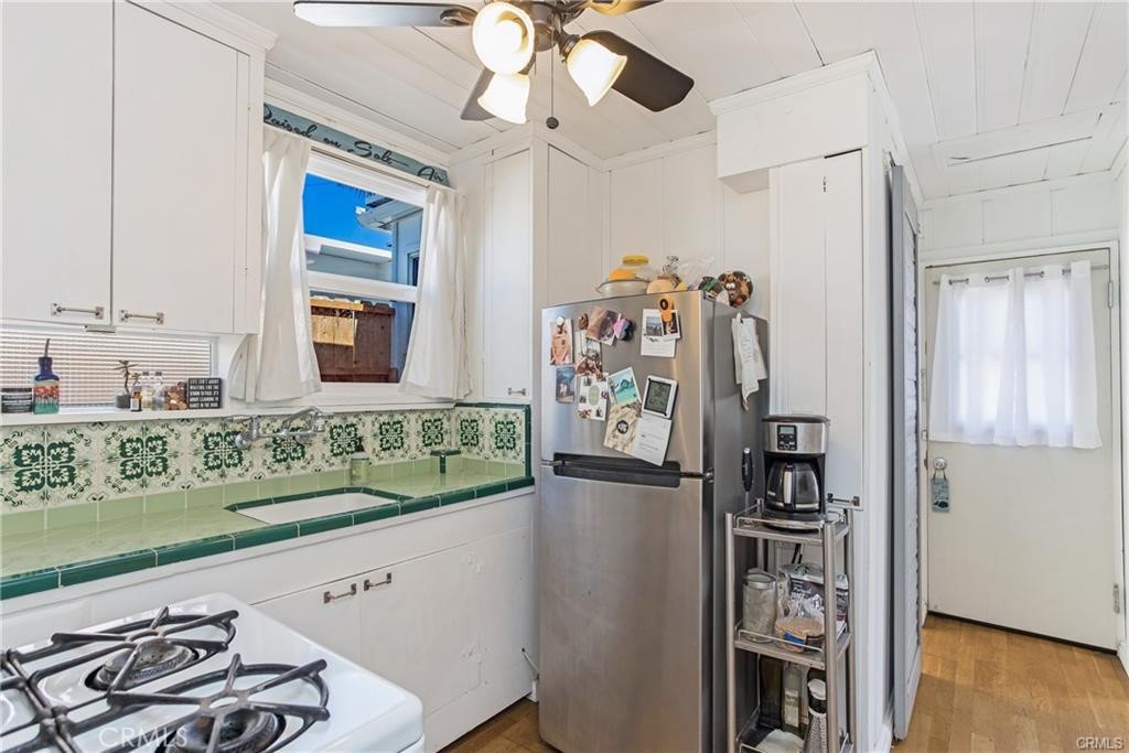 Compact kitchen with green tile counters and backsplash, white cabinets, and a stainless-steel refrigerator.