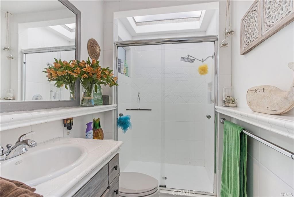 Bathroom with a glass shower, skylight, and tiled vanity.