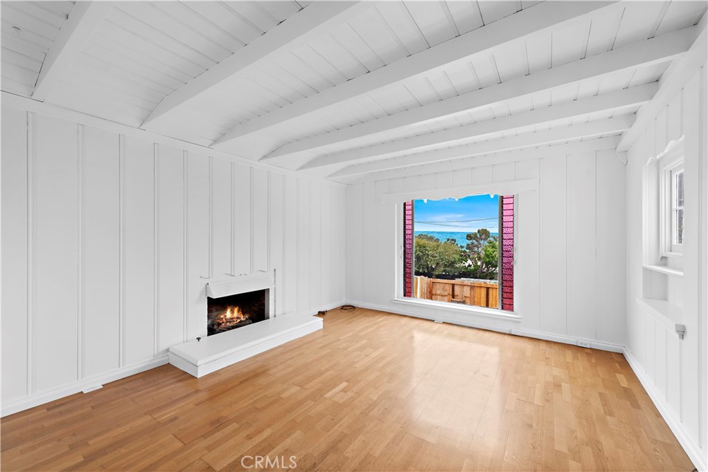 Vacant living room with white ceiling beams, a fireplace, wood floors, and an ocean view.