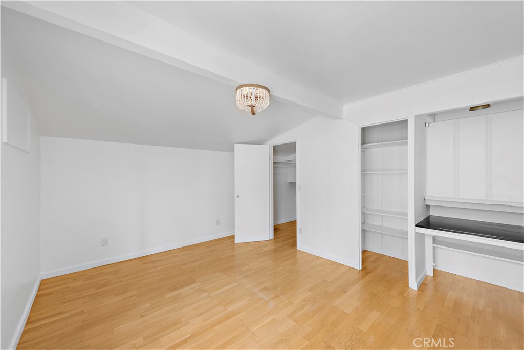 Vacant room with light hardwood floors, open closets, and a built-in desk.