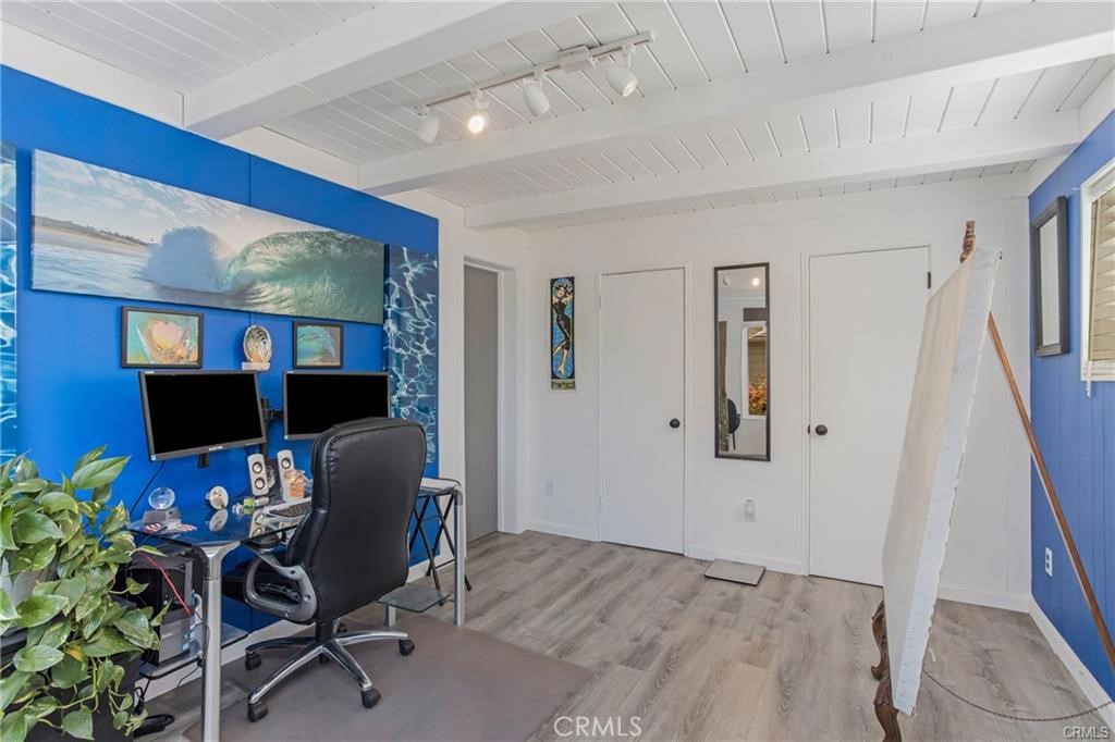 Furnished home office with dual monitors, a blue surf-art wall, and a surfboard.