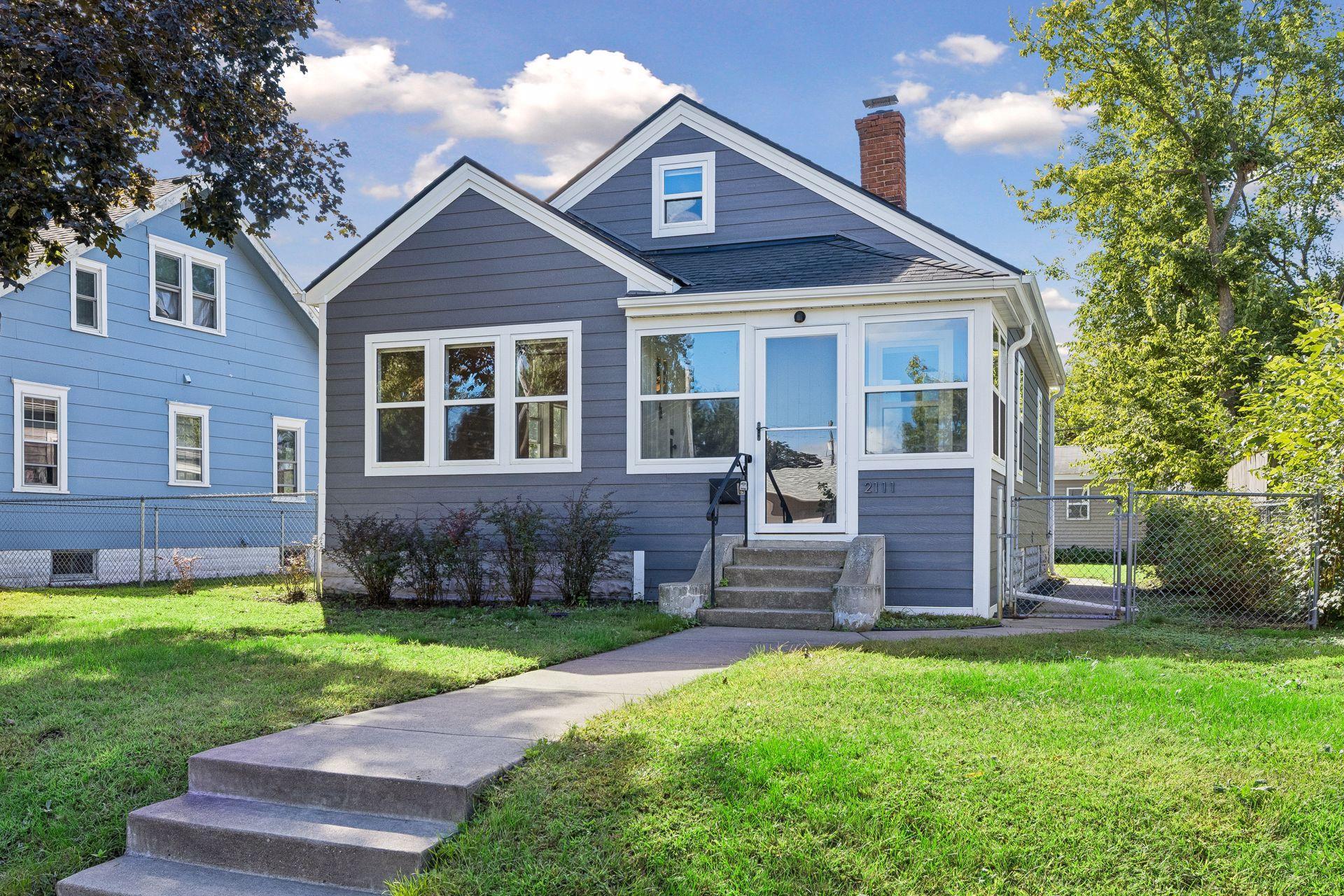 Gray gable-front house with white trim, concrete entry steps, and a fenced grassy yard.