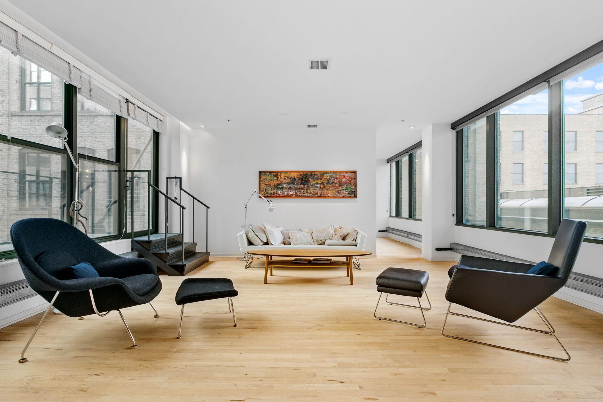 Modern loft living room with floor-to-ceiling windows, a metal staircase, and contemporary seating.
