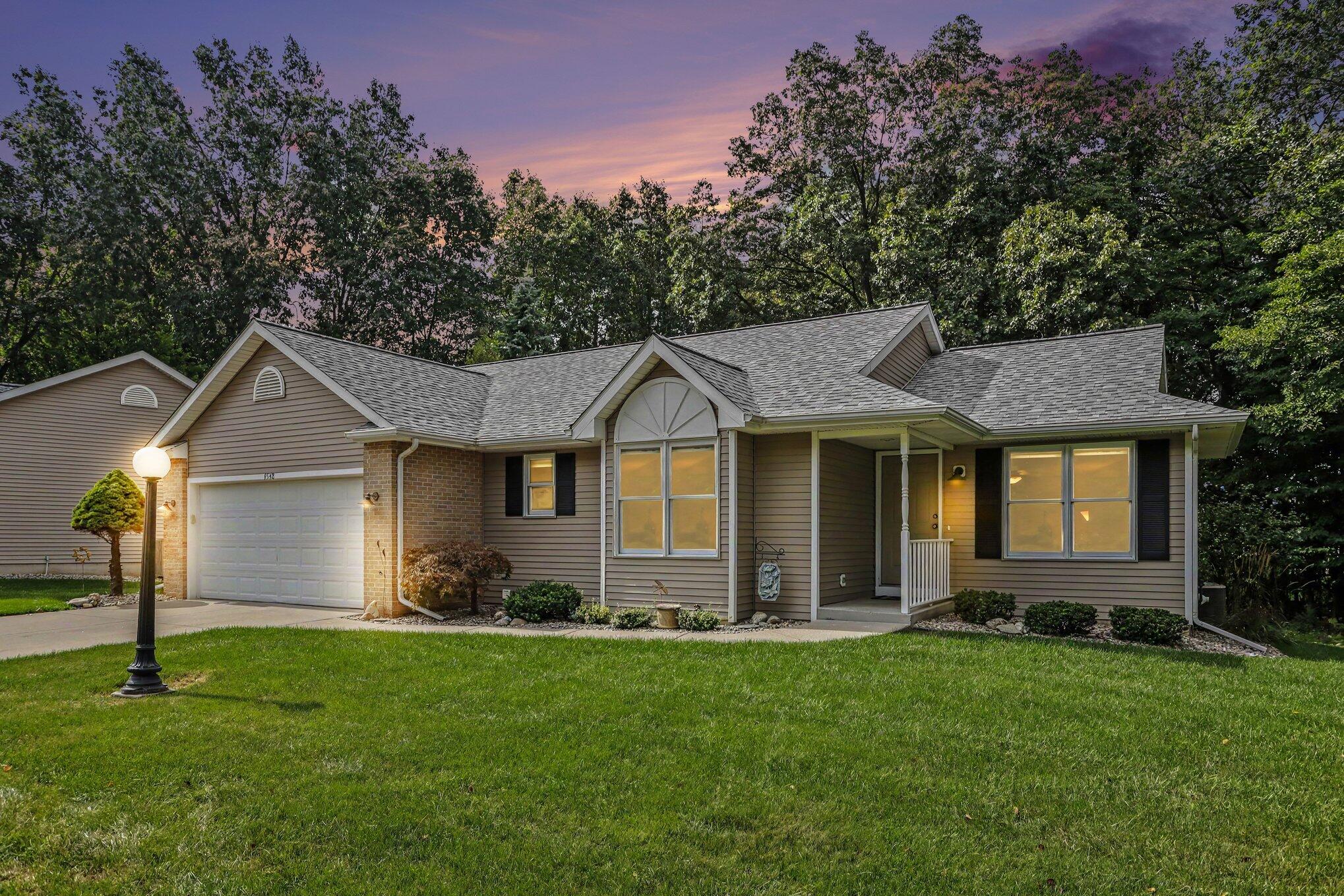 Single-story taupe-sided home with a two-car garage and covered entry, framed by a lawn at dusk.