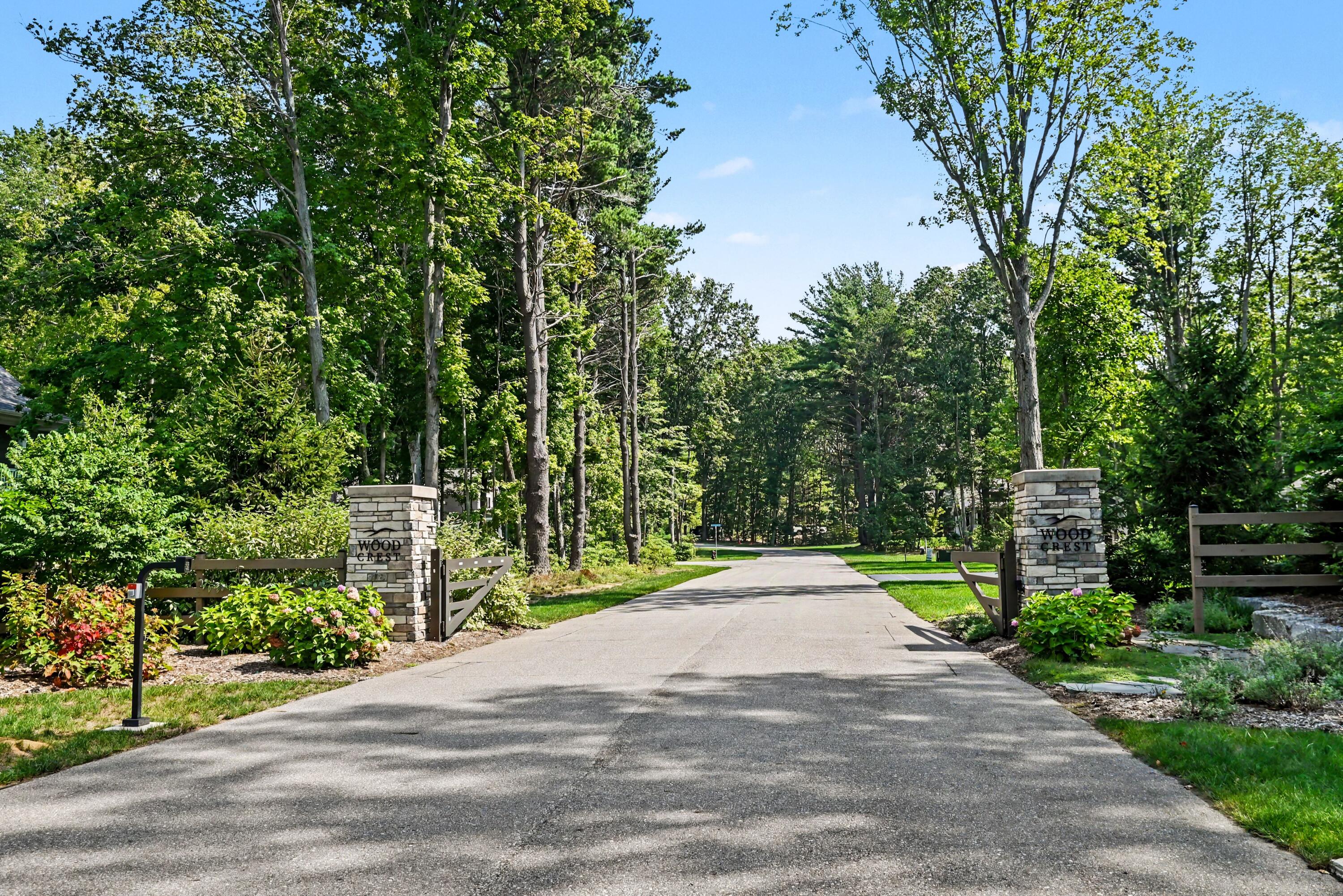 Tree-lined Wood Crest entrance road framed by stone pillars and open wooden gates.