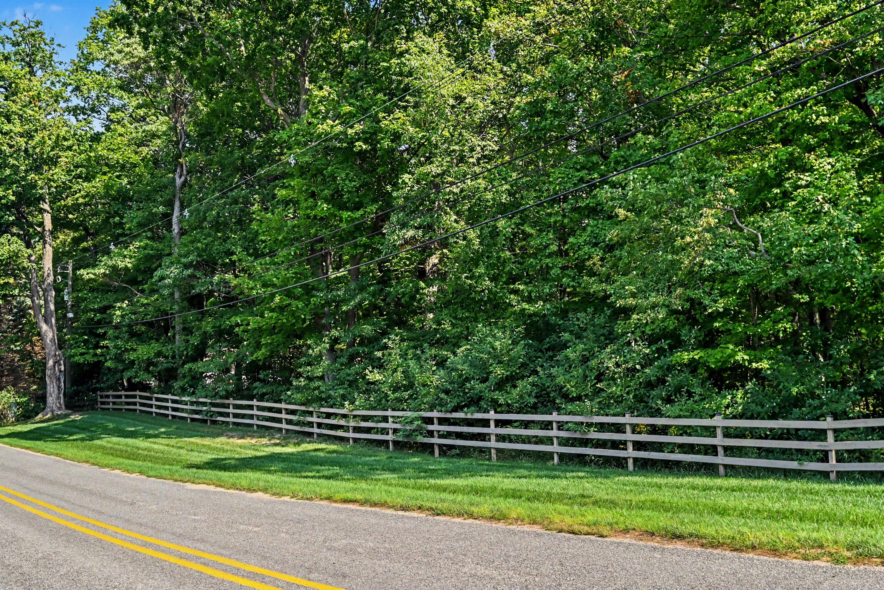 Wooded property bordered by a split-rail fence beside a two-lane road.