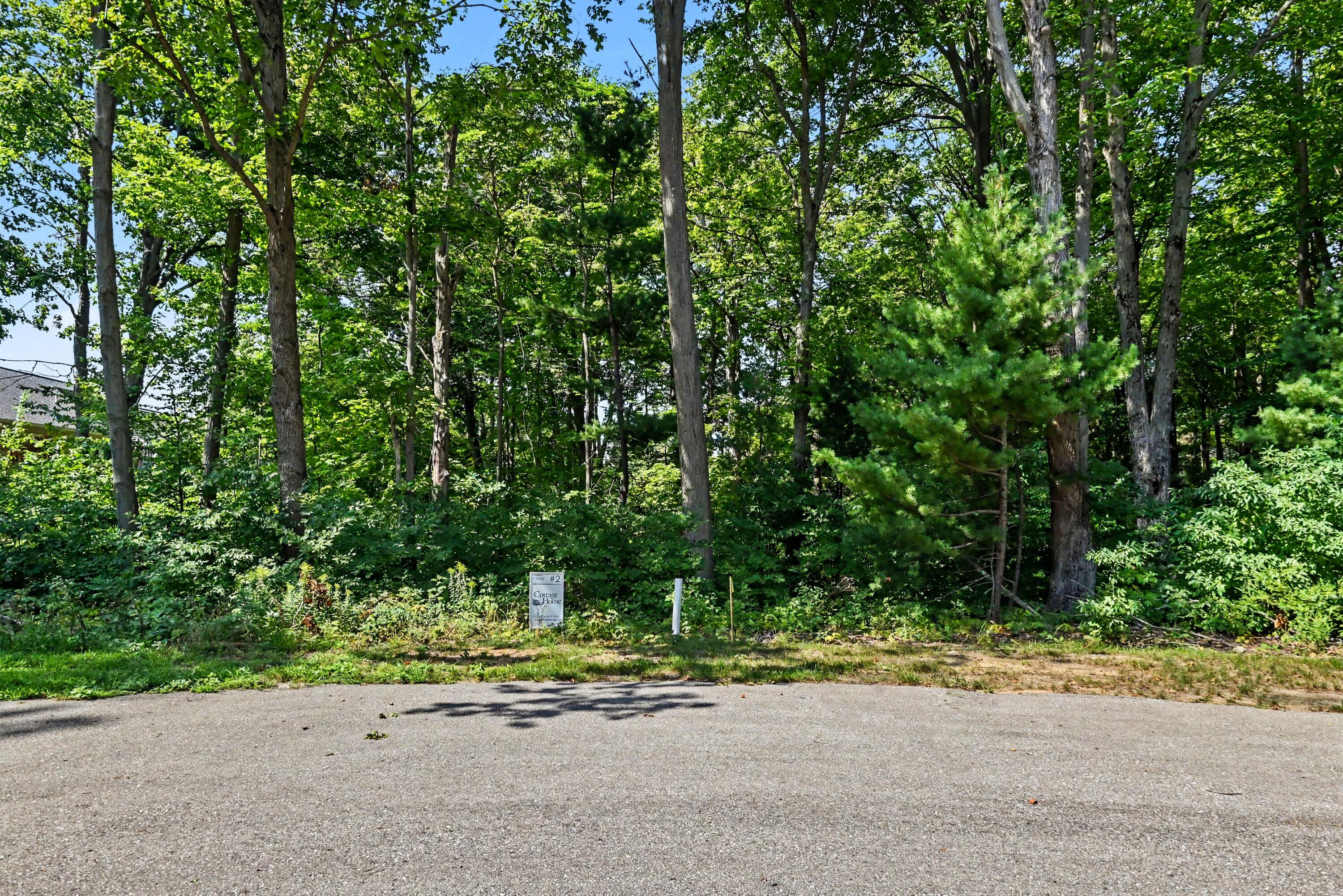 Wooded property lot beside a paved road, marked with a Cottage Home real estate sign.