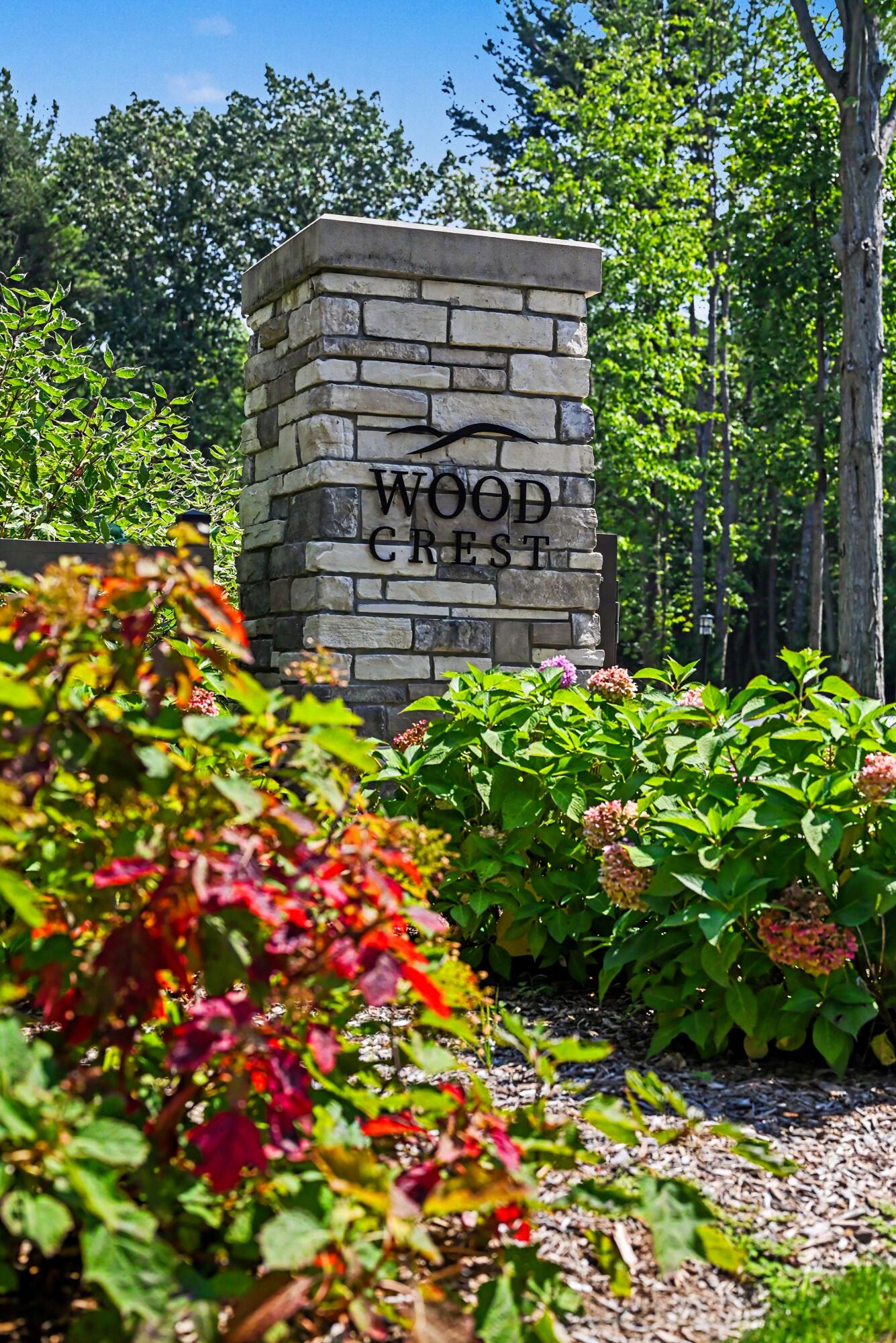 Wood Crest community entrance sign surrounded by flowering shrubs and trees.