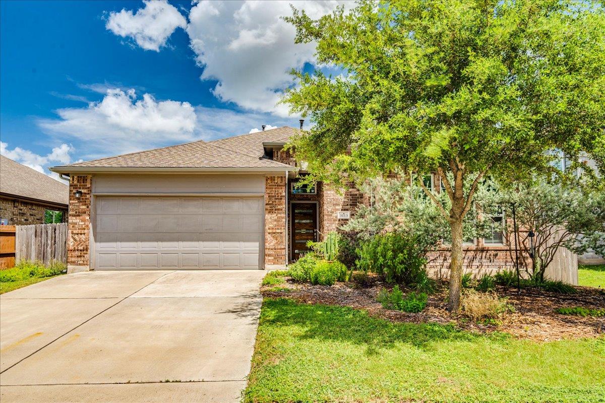 Brick home with a two-car garage, wide driveway, and mature shade tree in the front yard.