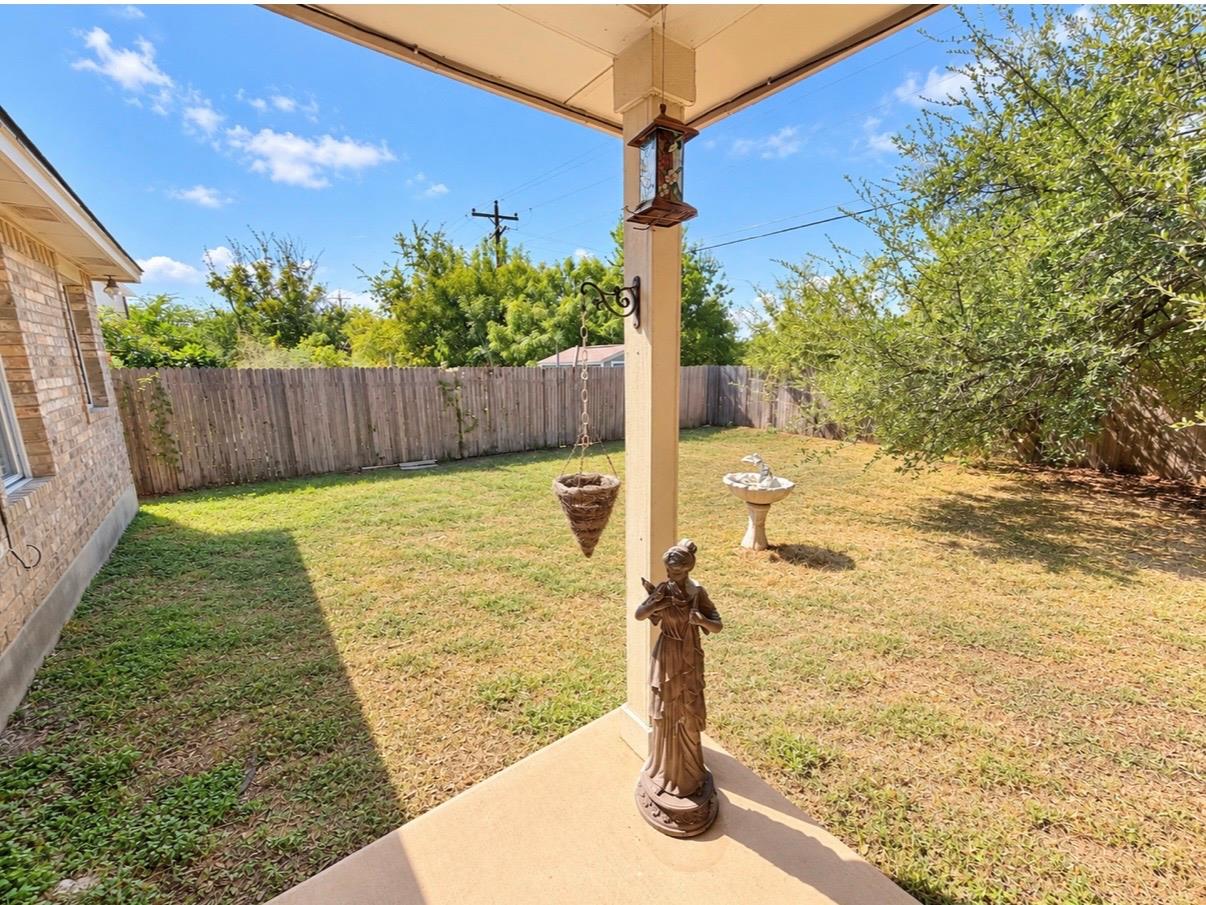 Covered patio overlooking a fenced grassy backyard with mature trees and a birdbath.