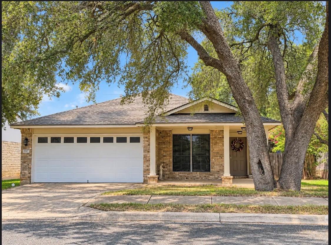 Brick house with a two-car garage and covered entry beneath large oak trees.