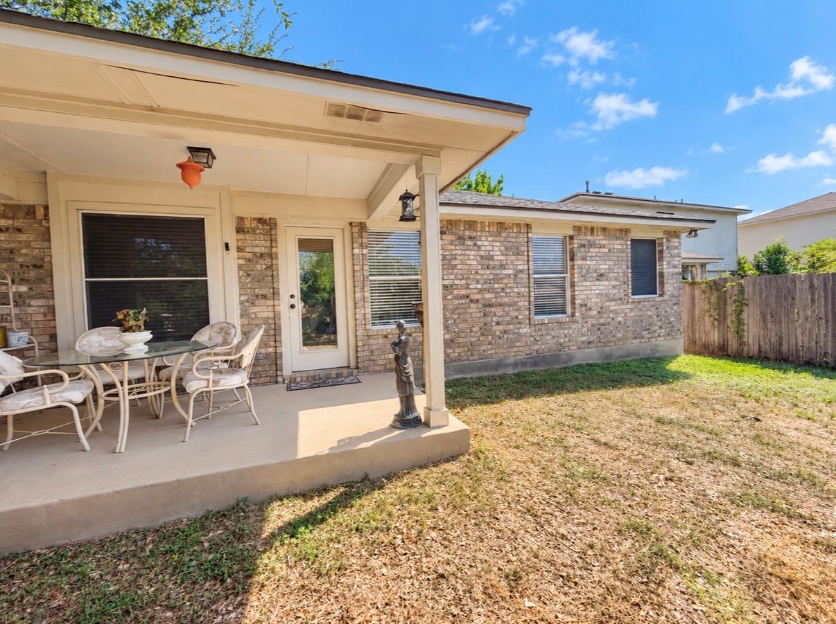 Brick home's covered rear patio with dining set, overlooking a small fenced backyard.