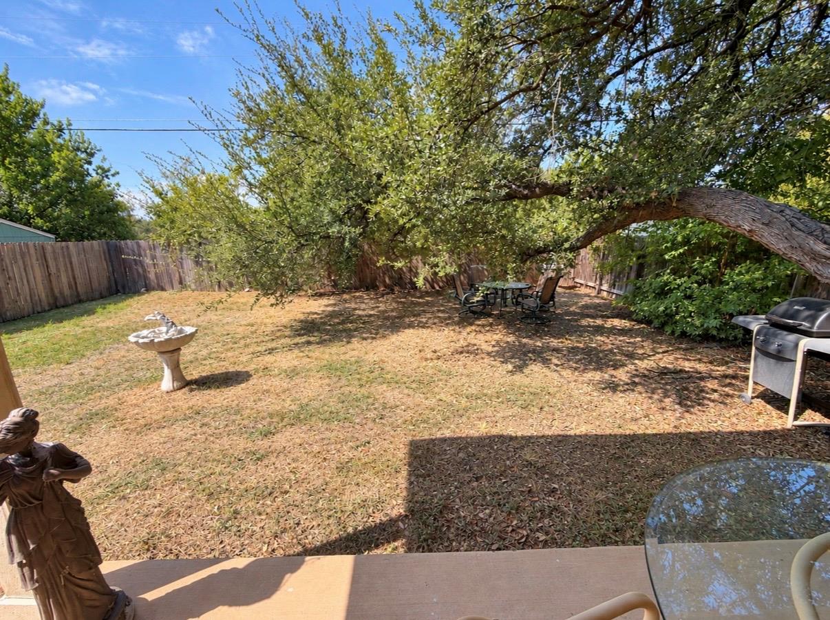Fenced backyard with a large shade tree, patio seating, grill, and birdbath.