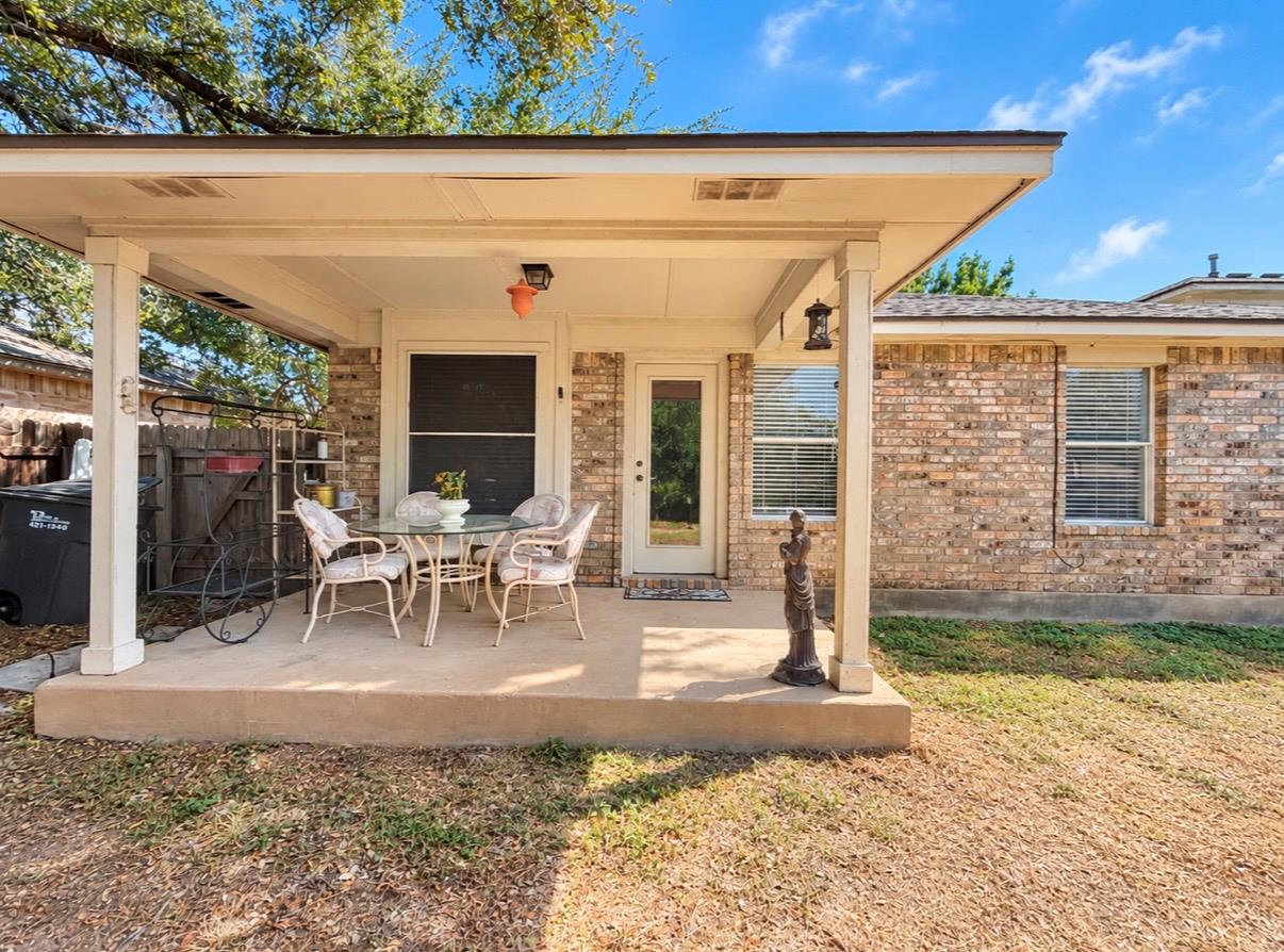 Covered concrete patio with a white outdoor dining set beside a brick home.