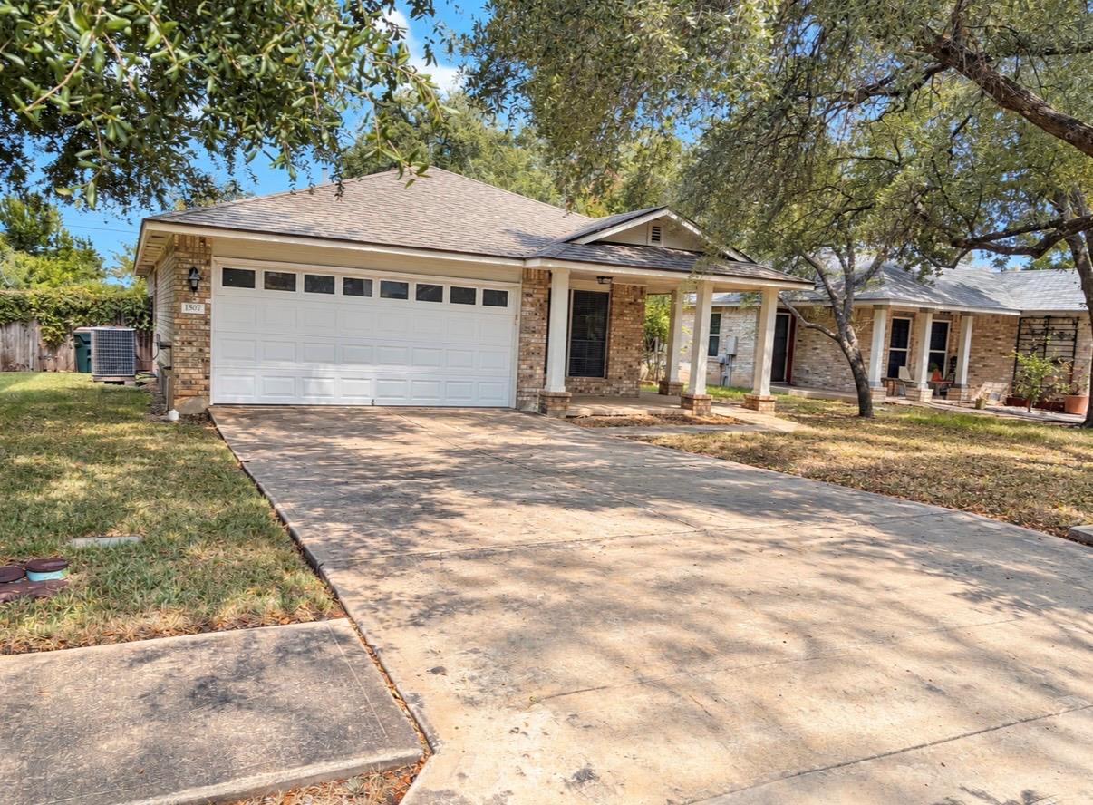 Brick house with a two-car garage and broad driveway beneath mature shade trees.