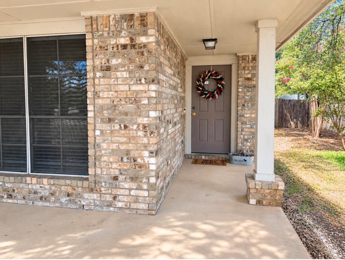 Brick house entry with a gray front door, wreath, and covered concrete porch.