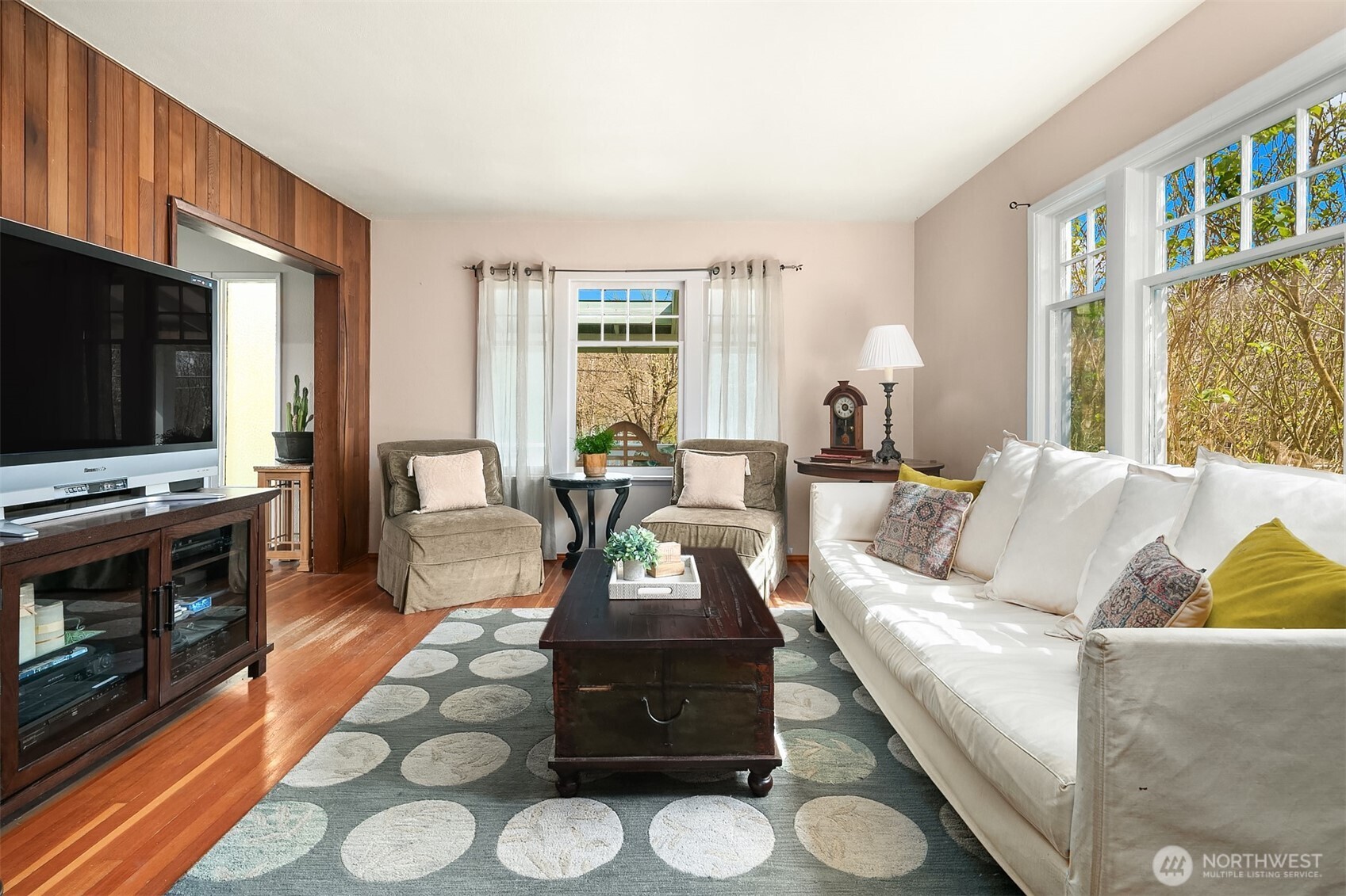 Furnished living room with a wood-paneled wall, white sofa, patterned rug, and large windows.