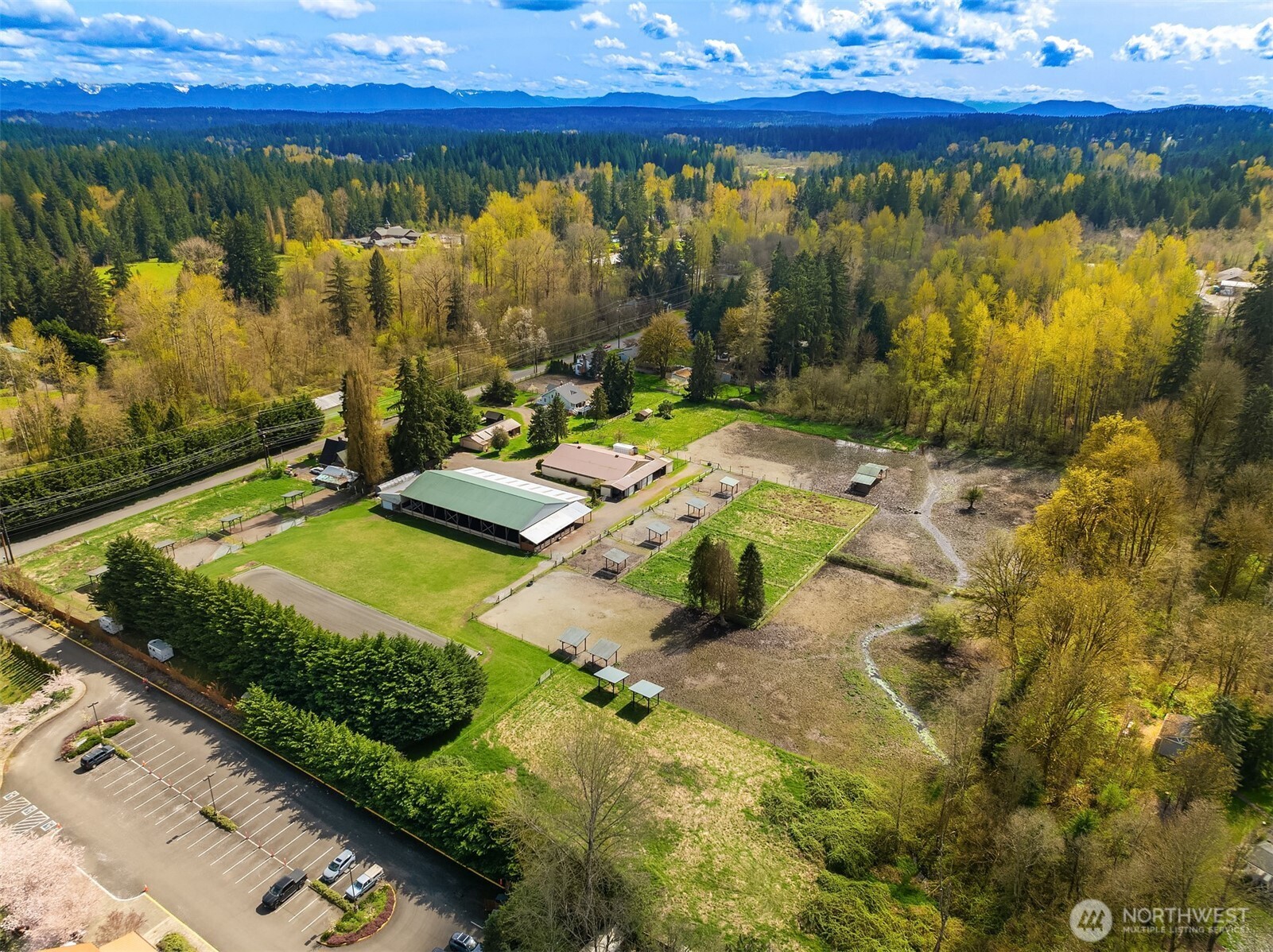 Aerial property view with a large barn, fenced paddocks, open fields, and distant mountains.