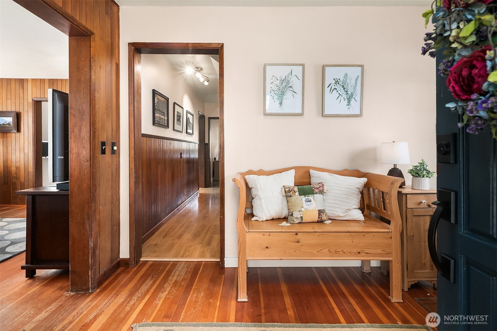 Home entry with a wooden settee, rich wood floors, and a hallway with wood-paneled wainscoting.