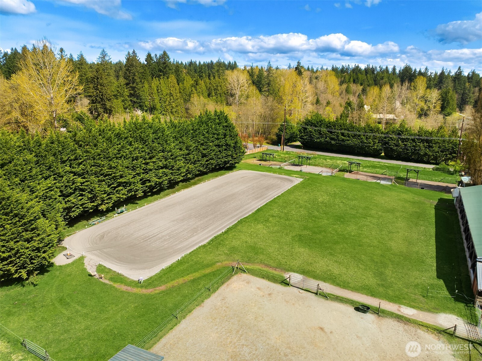 Aerial view of an equestrian property with an oval riding arena, fenced paddocks, and a barn.
