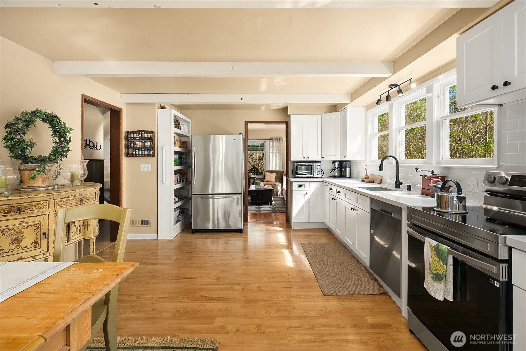 Bright kitchen with white cabinetry, stainless steel appliances, hardwood floors, and large windows.
