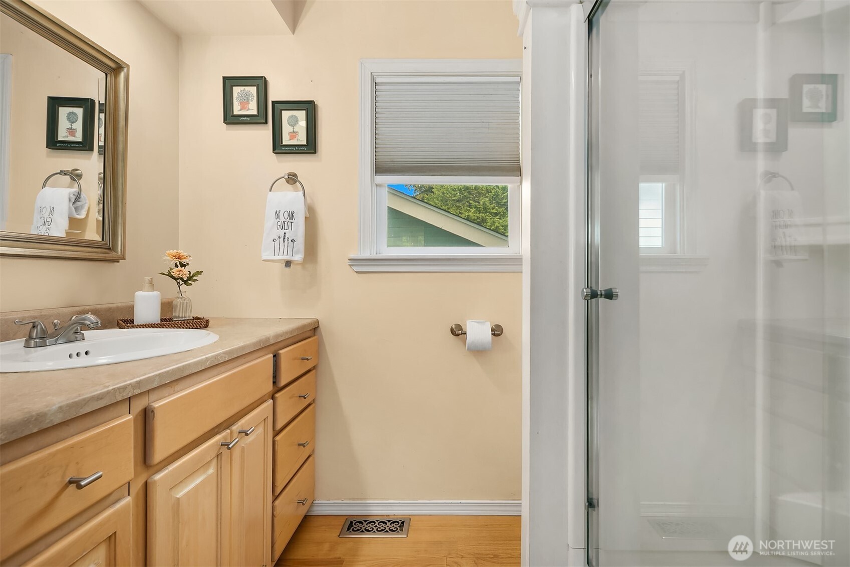 Bathroom with a wood vanity, beige countertop, window, and glass-enclosed shower.