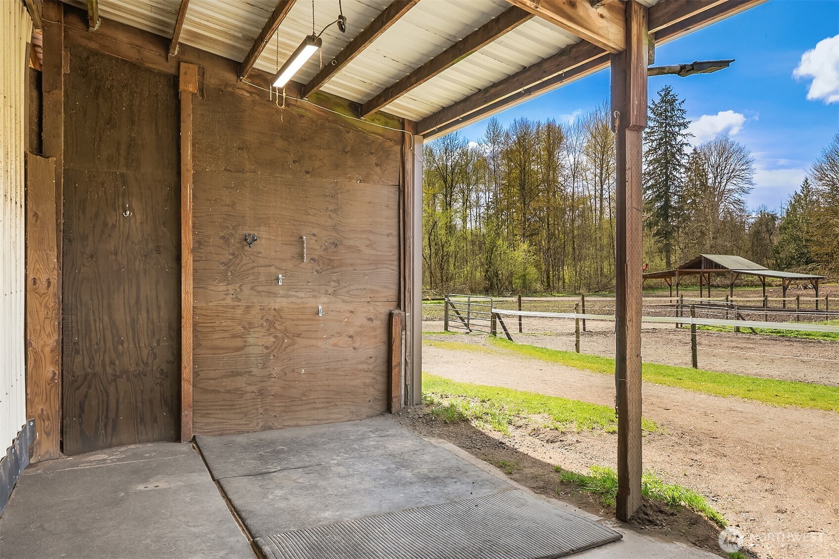 Open-sided wooden stable bay overlooks fenced paddocks and a covered shelter.
