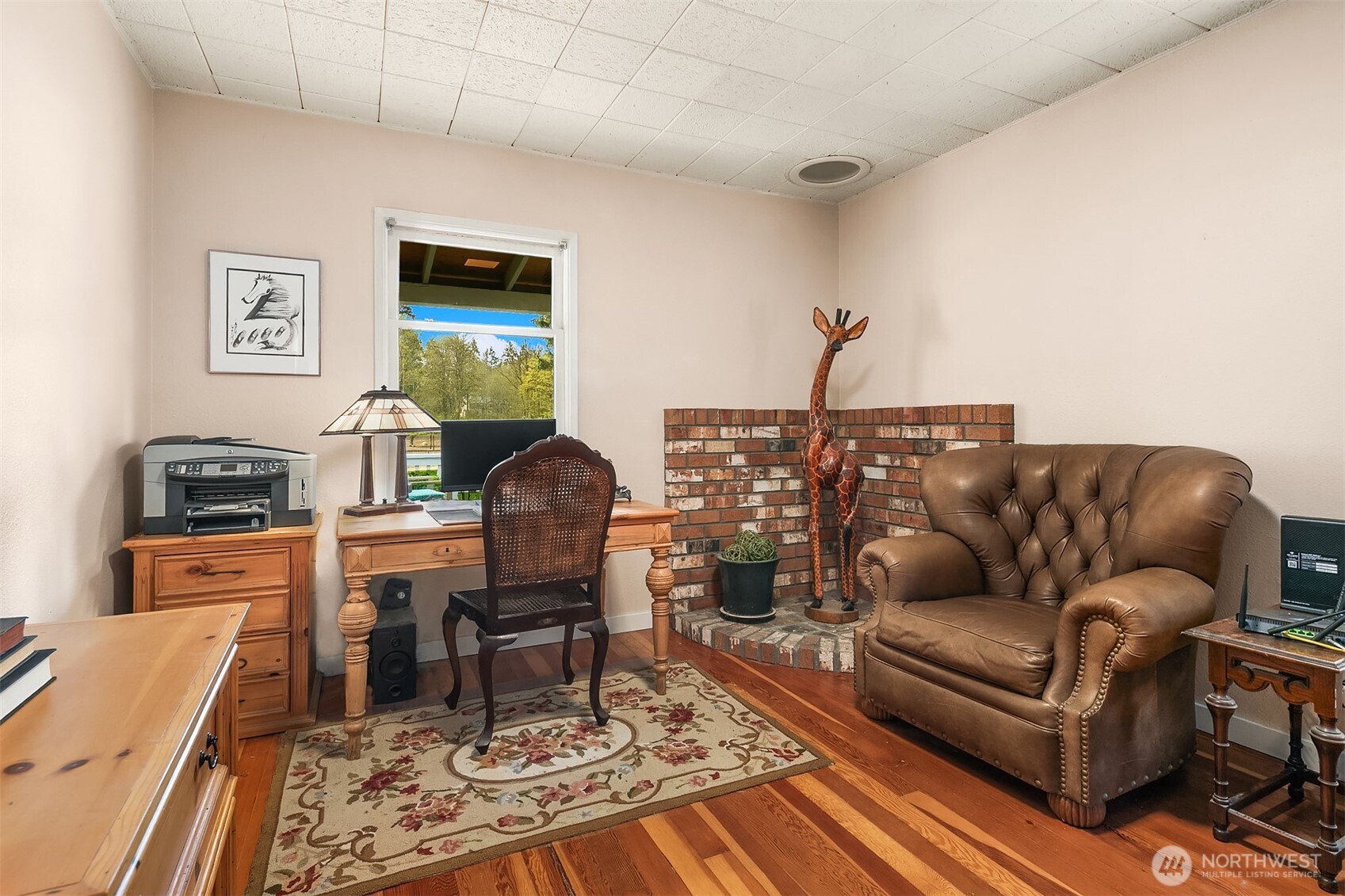 Furnished home office with a brick fireplace, wooden desk, and leather armchair.