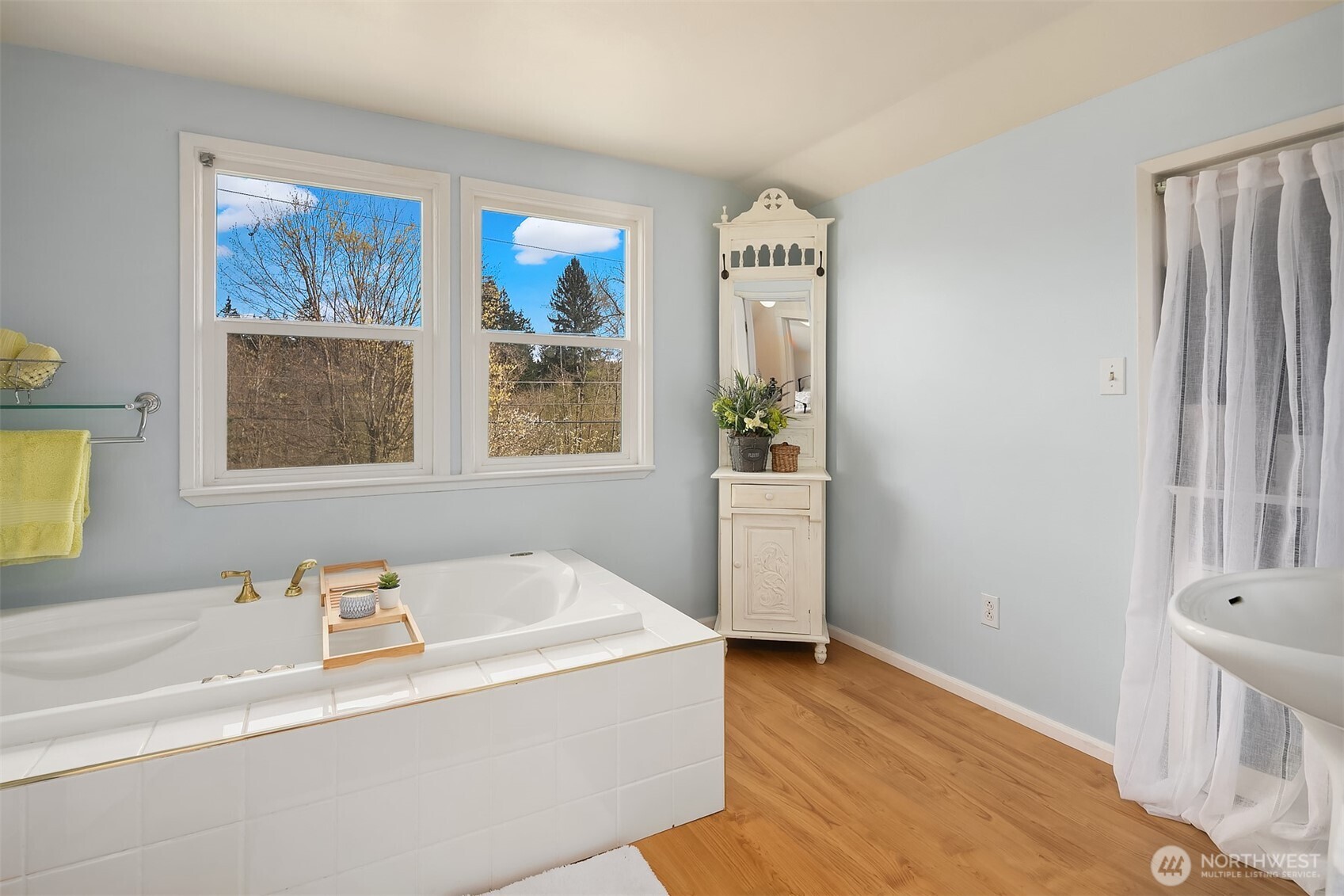 Bathroom with a built-in soaking tub, two large windows, and warm wood flooring.