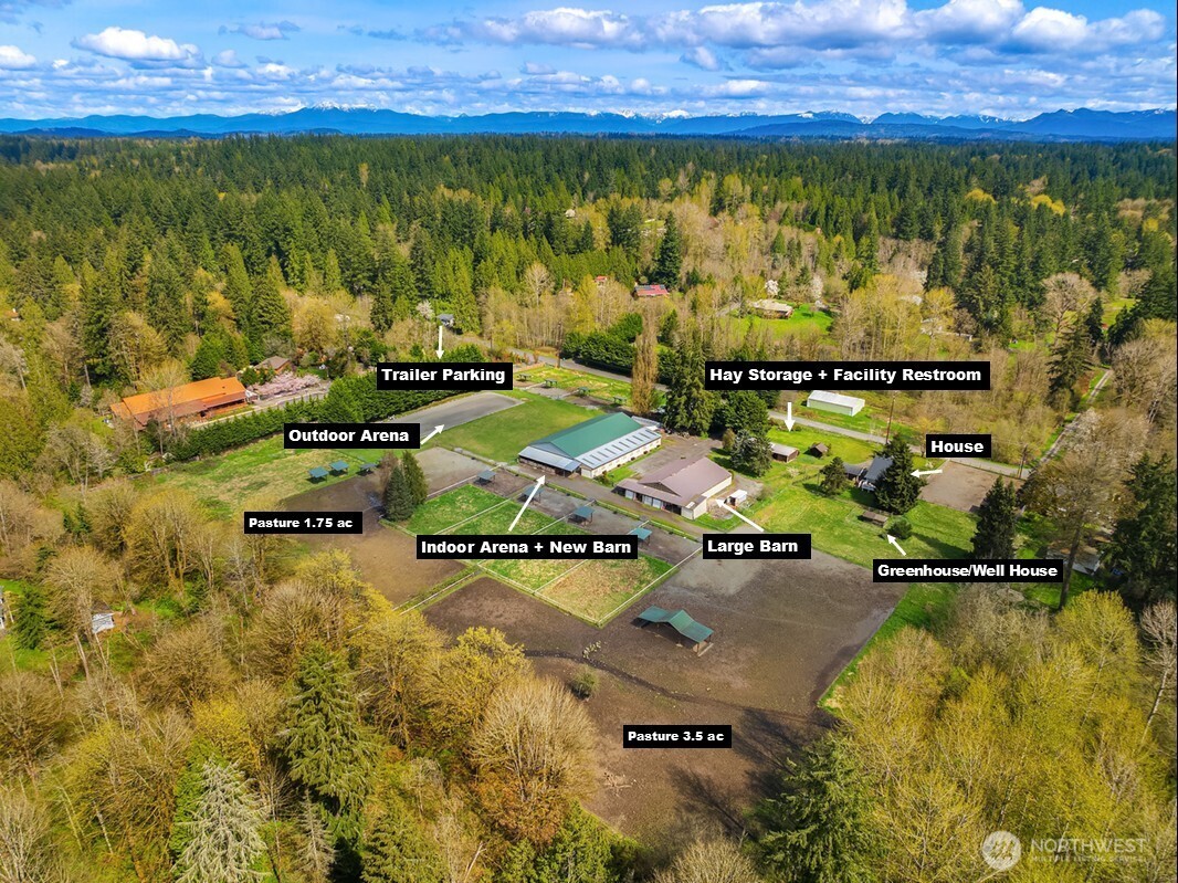 Aerial view of an equestrian property with barns, riding arenas, pastures, and forested mountain views.