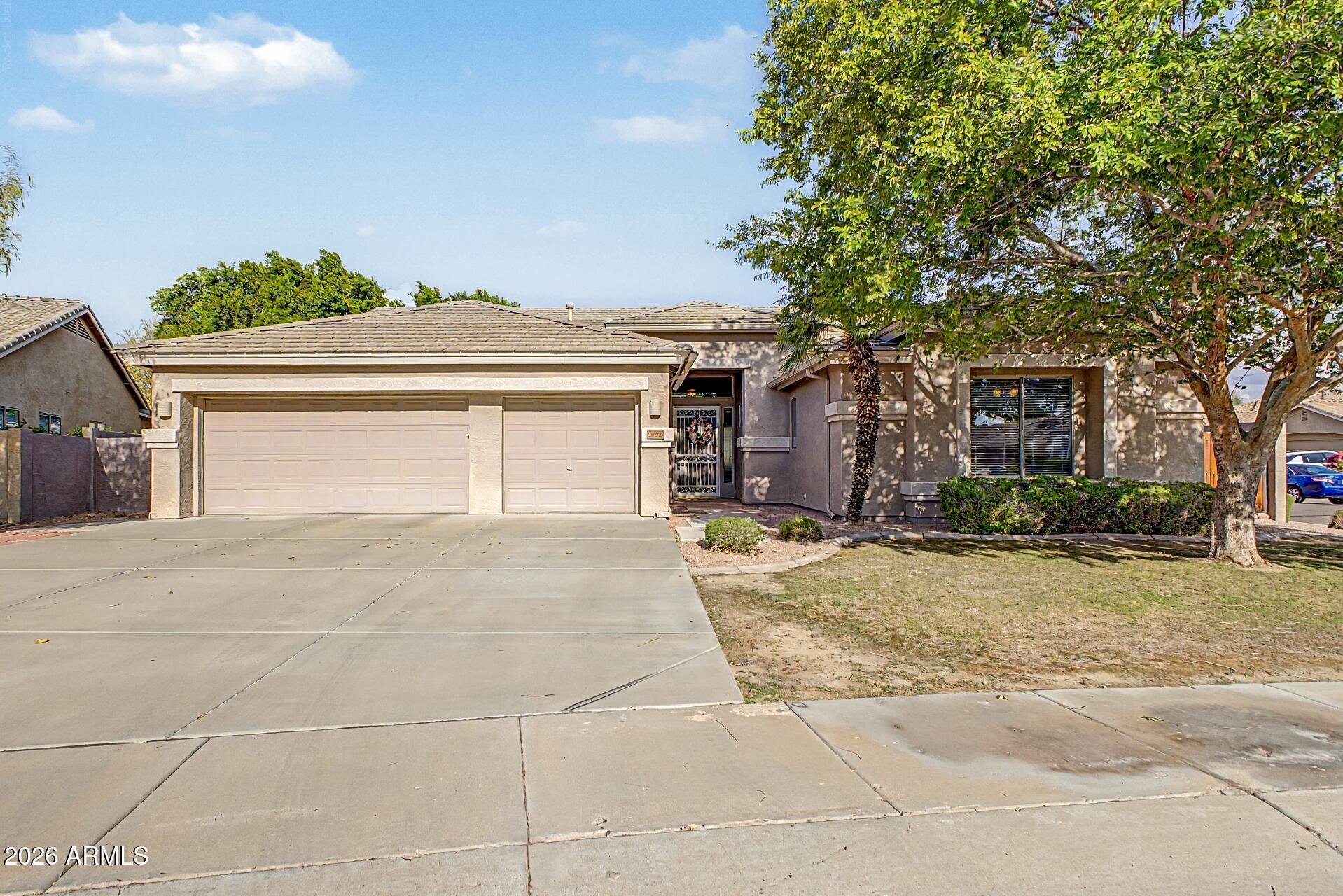 Single-story stucco house with a two-car garage, wide driveway, and large shade tree.