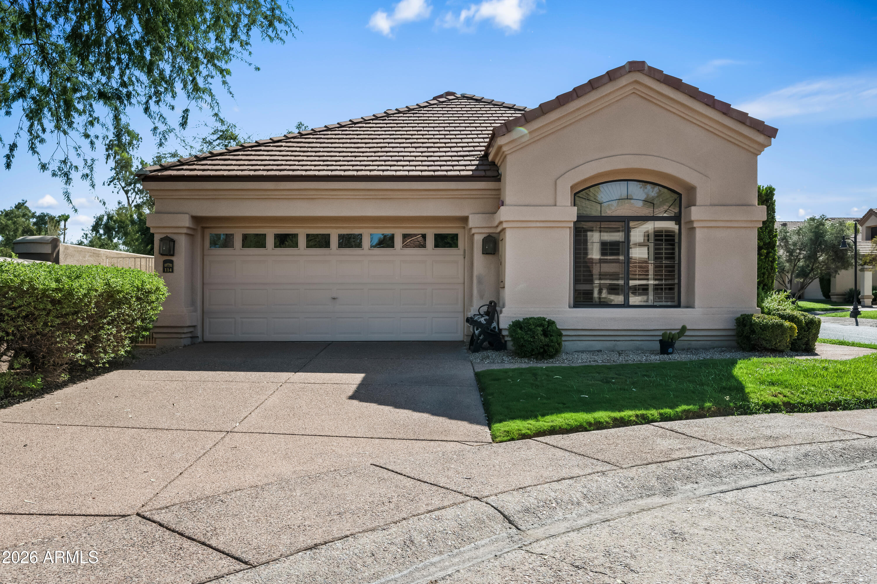 Tan stucco home with a tiled roof, two-car garage, and large arched front window.