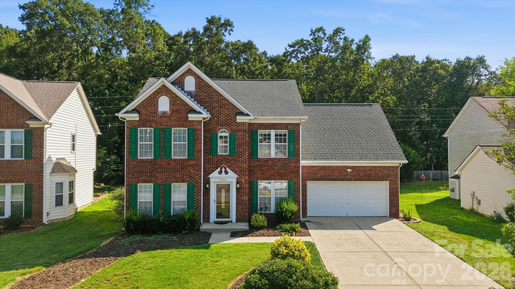 Two-story red brick house with green shutters, an attached garage, and a wide concrete driveway.