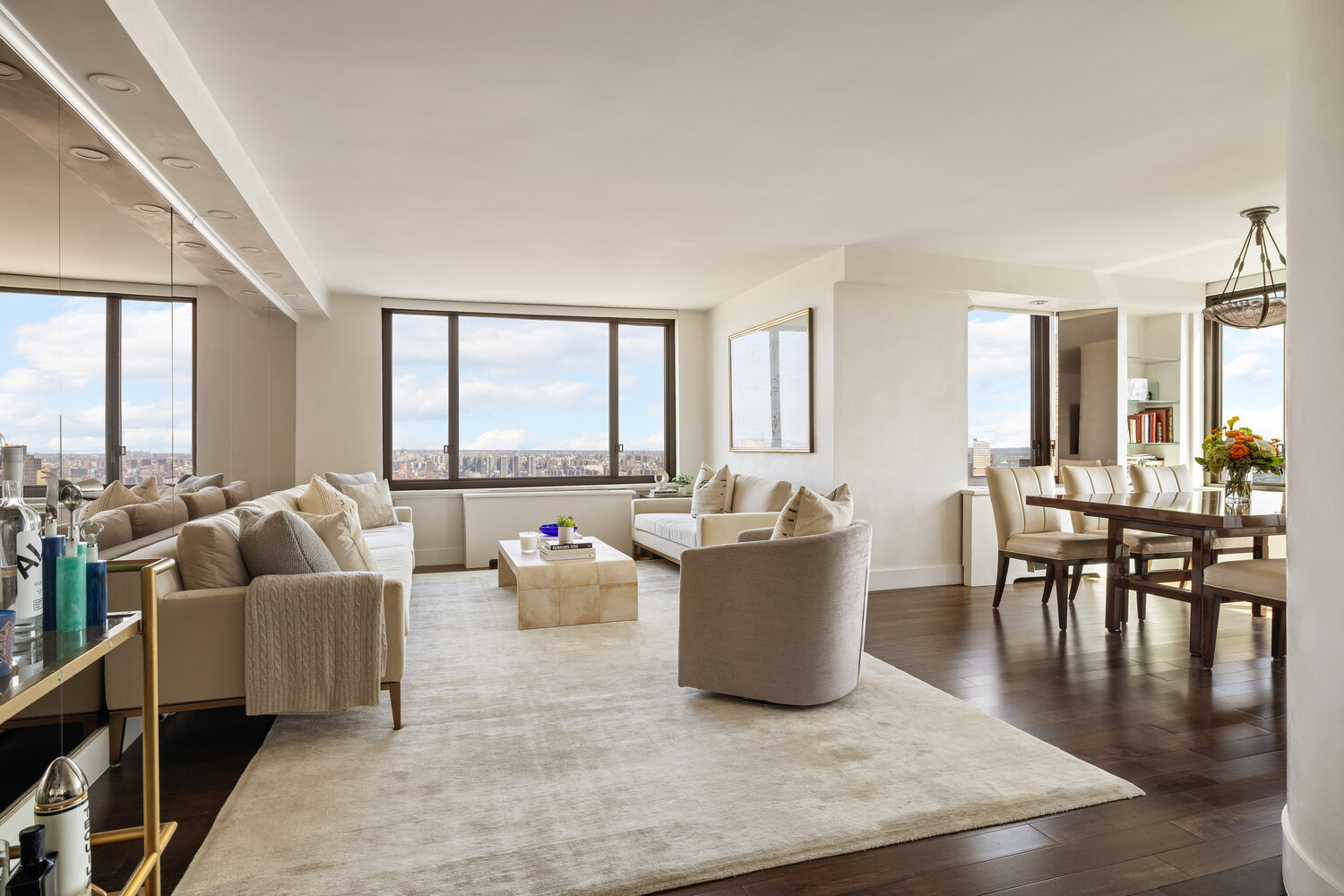 Open-plan living and dining room with neutral furnishings and floor-to-ceiling city-view windows.