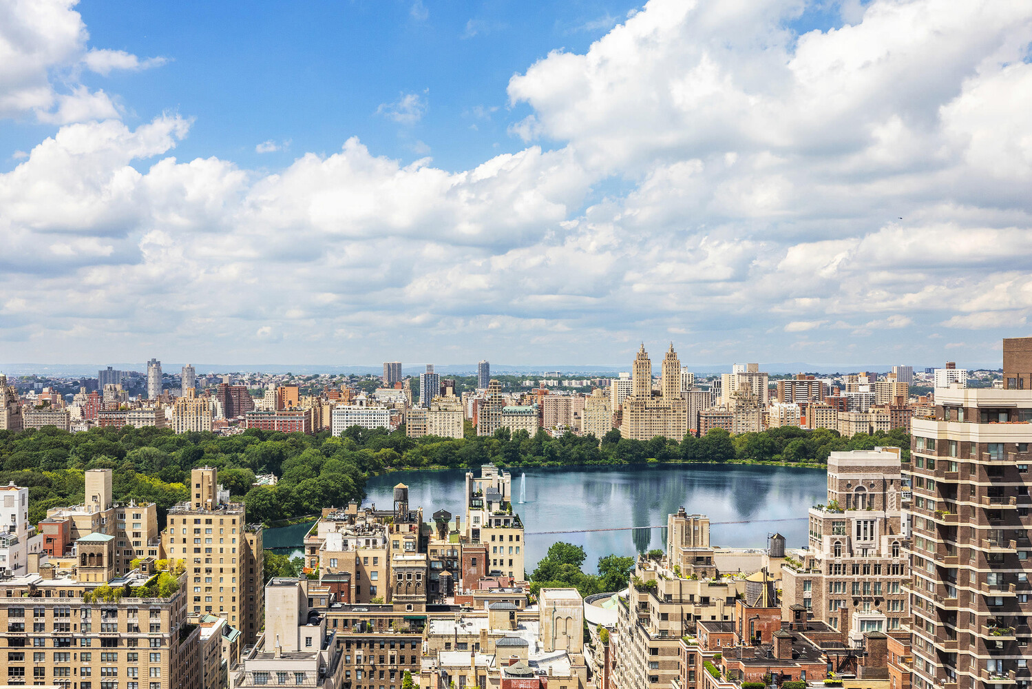 Upper East Side skyline and Central Park reservoir beneath a bright, cloud-filled sky.
