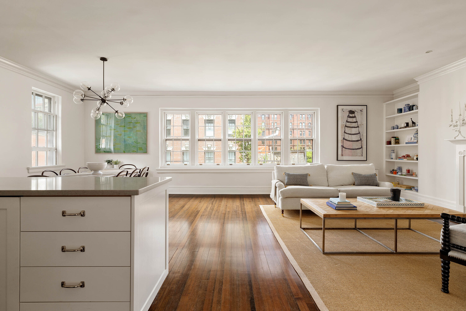 Open-plan living and dining room with a kitchen island, hardwood floors, and large windows.