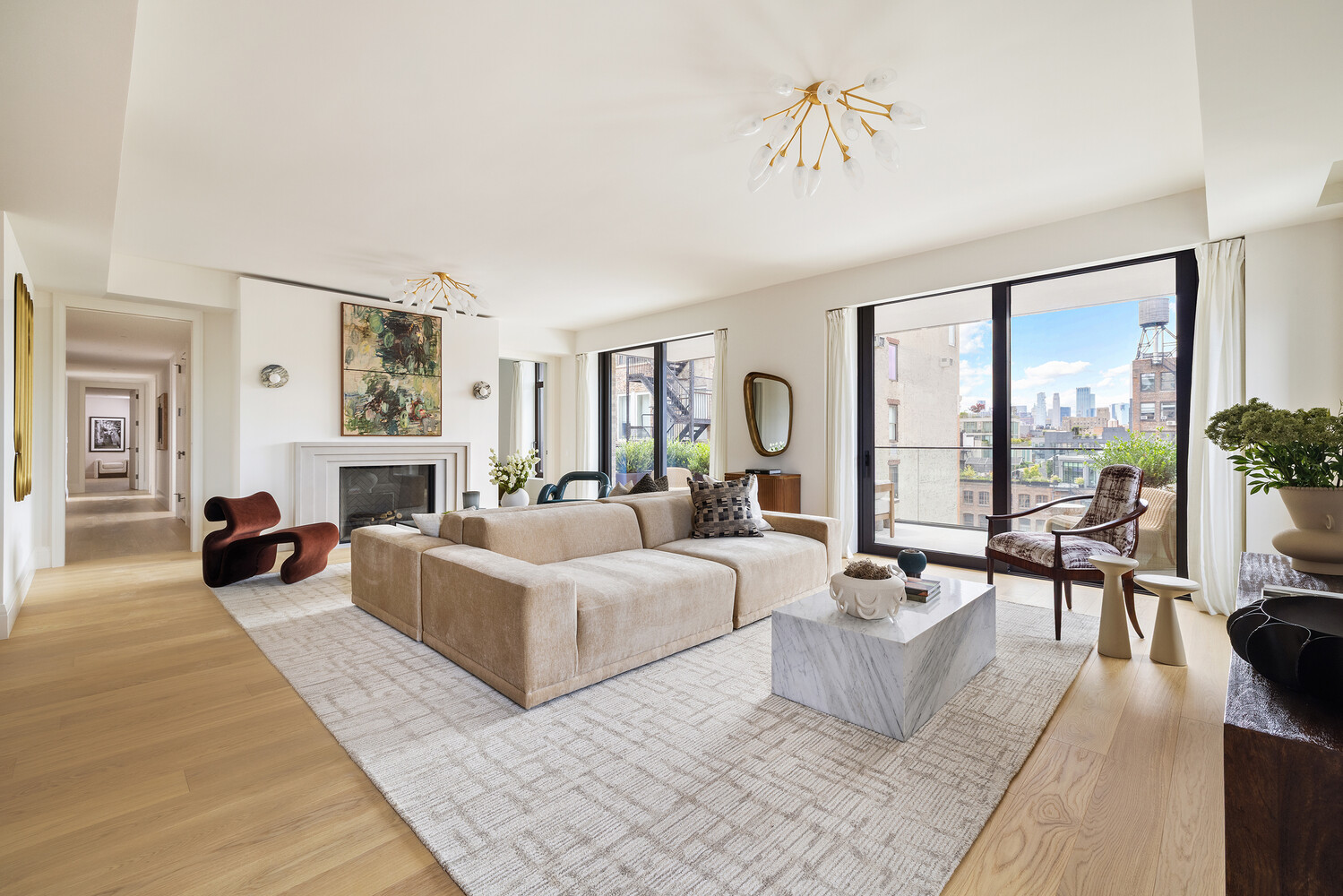 Bright living room with a sculptural sofa, fireplace, and city views through floor-to-ceiling windows.