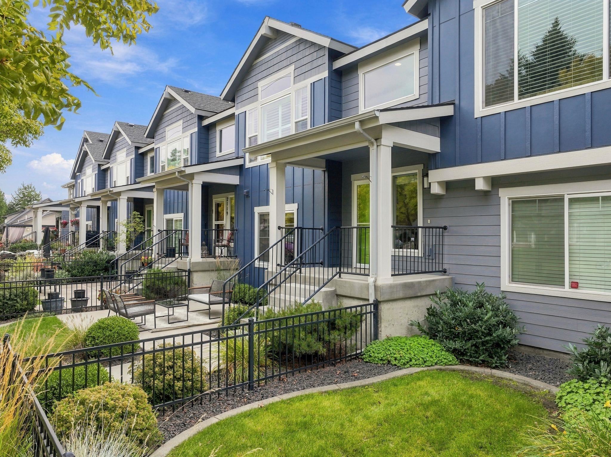 Blue and gray townhomes with covered porches, black railings, and landscaped front gardens.