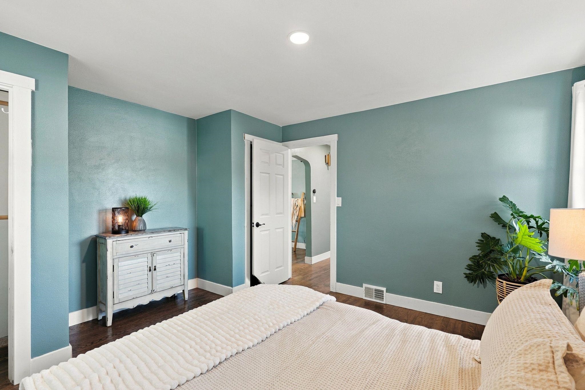 Bedroom with teal walls, a white bed, dark wood floors, and a distressed white dresser.