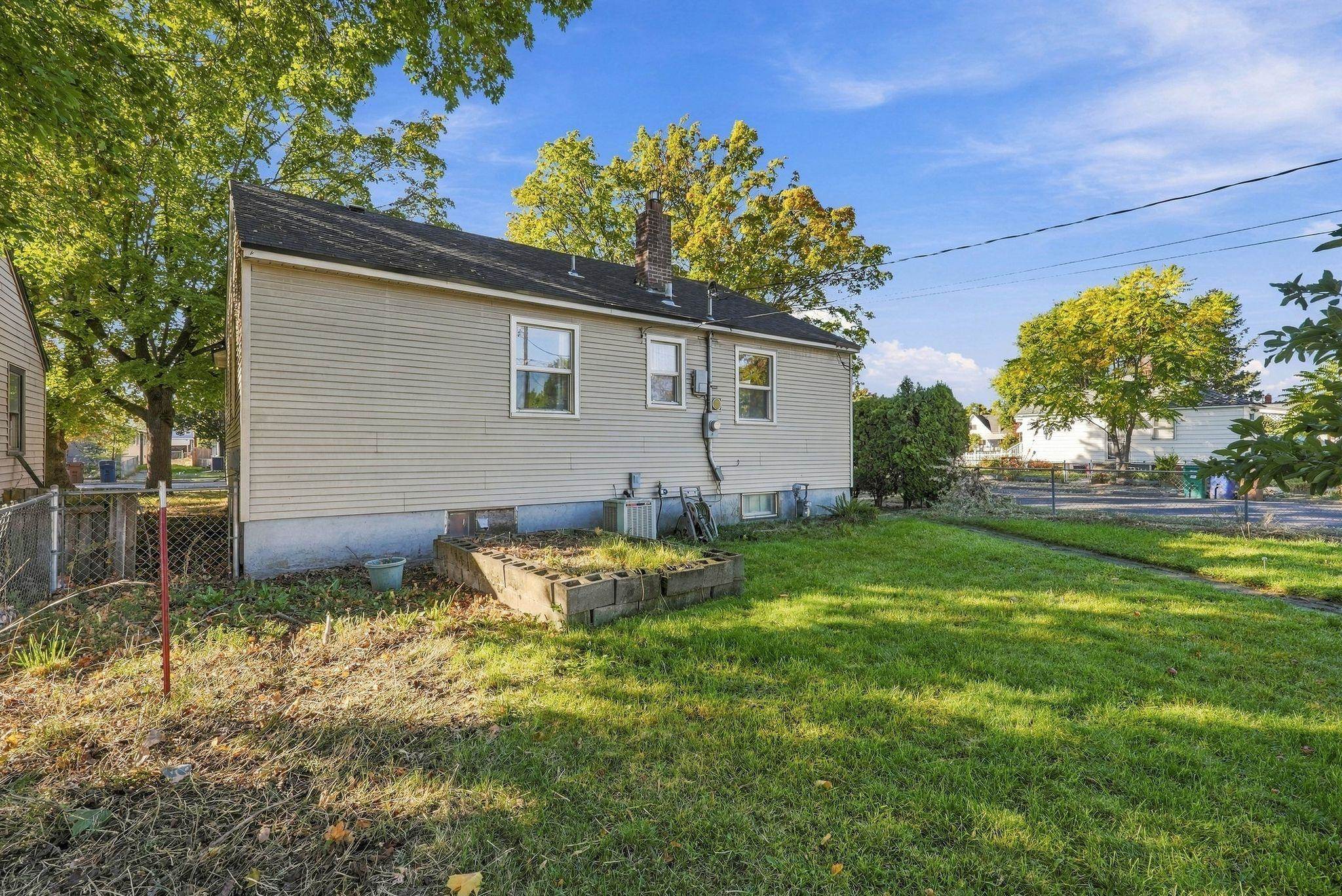 Side of a beige house beside a grassy backyard with a raised garden bed and chain-link fence.