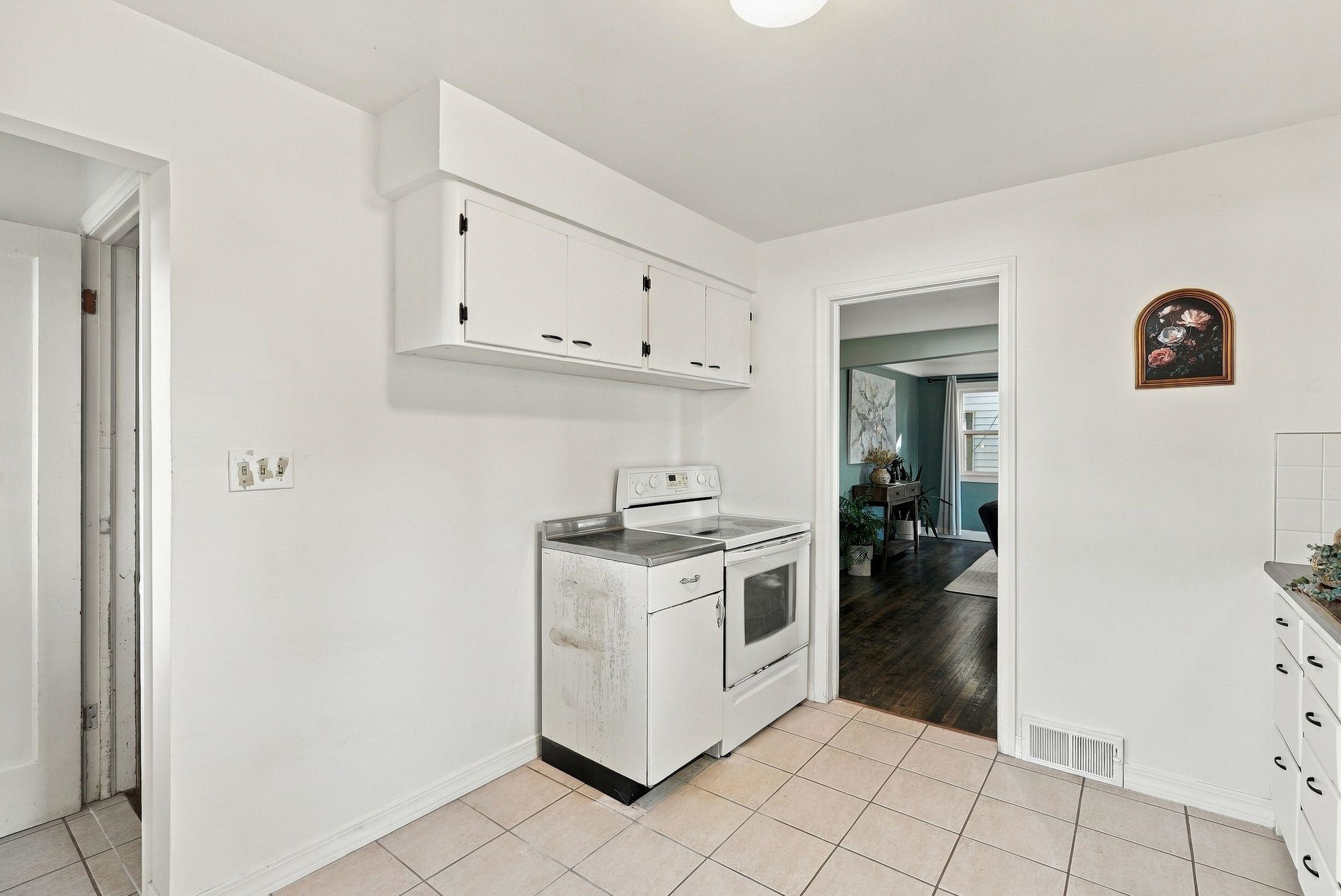 Laundry area with white cabinets, a washer, an electric range, and tiled flooring.