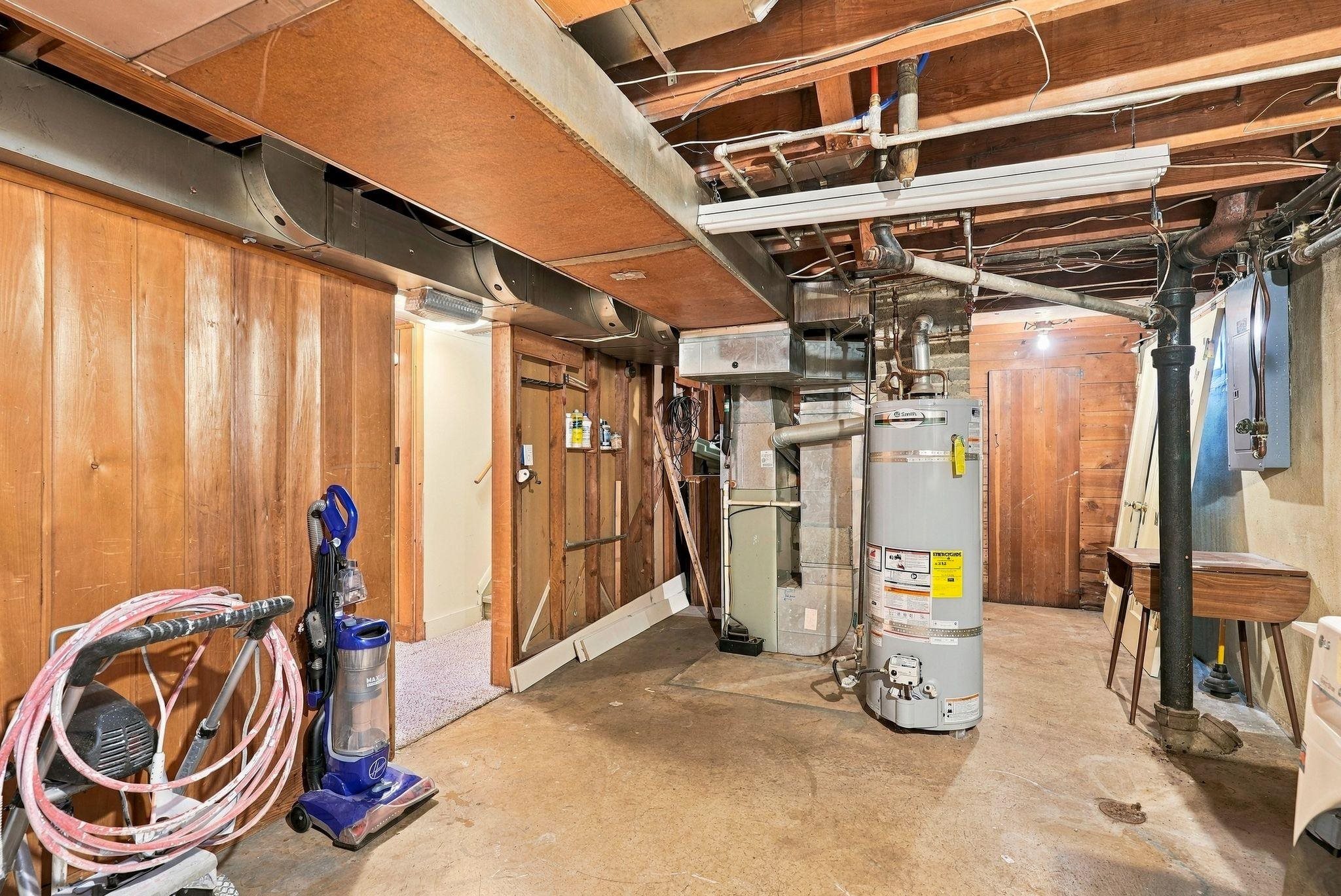 Unfinished basement utility area with exposed ductwork, a water heater, and wood-paneled walls.