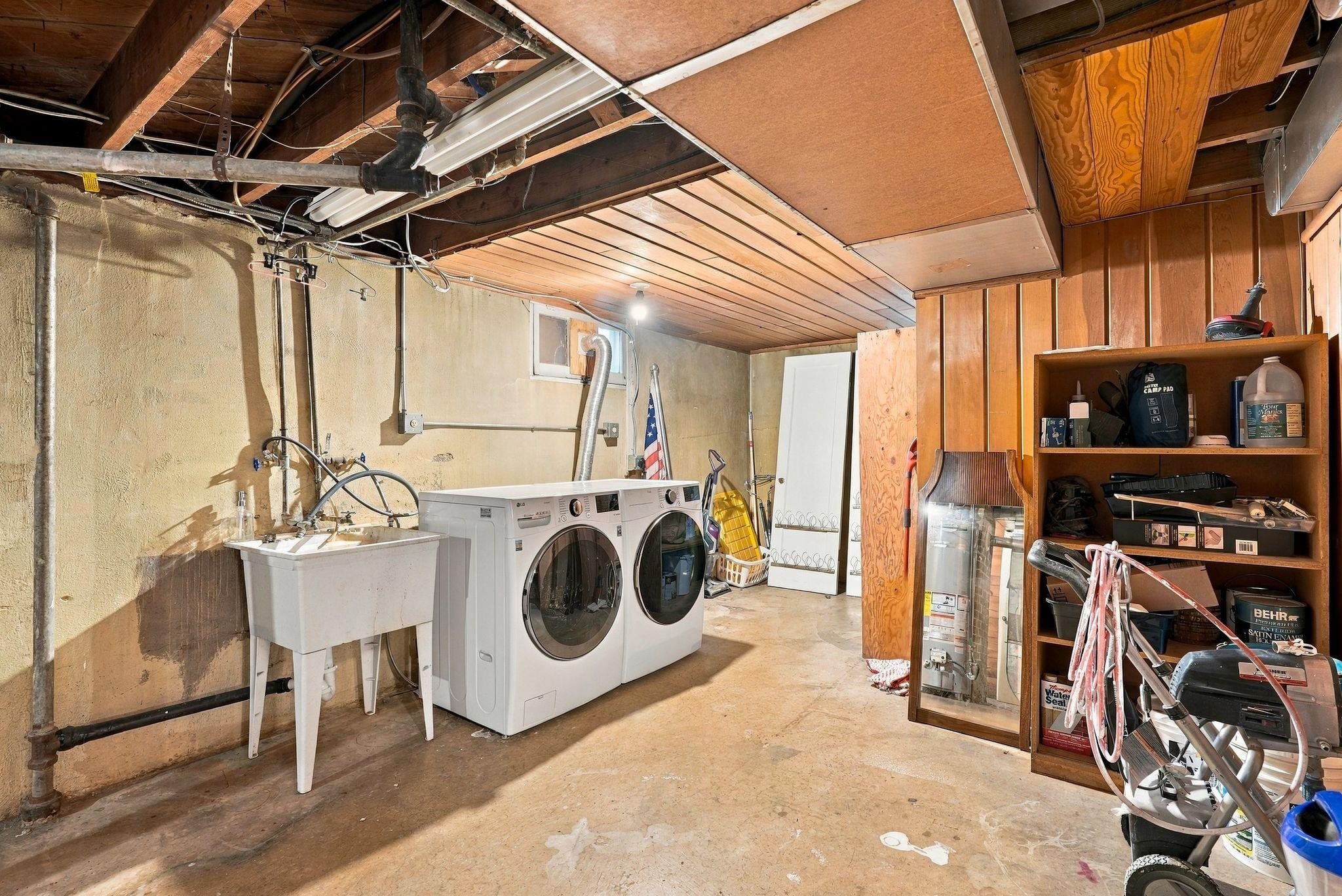 Basement laundry room with washer, dryer, utility sink, exposed pipes, and storage shelves.